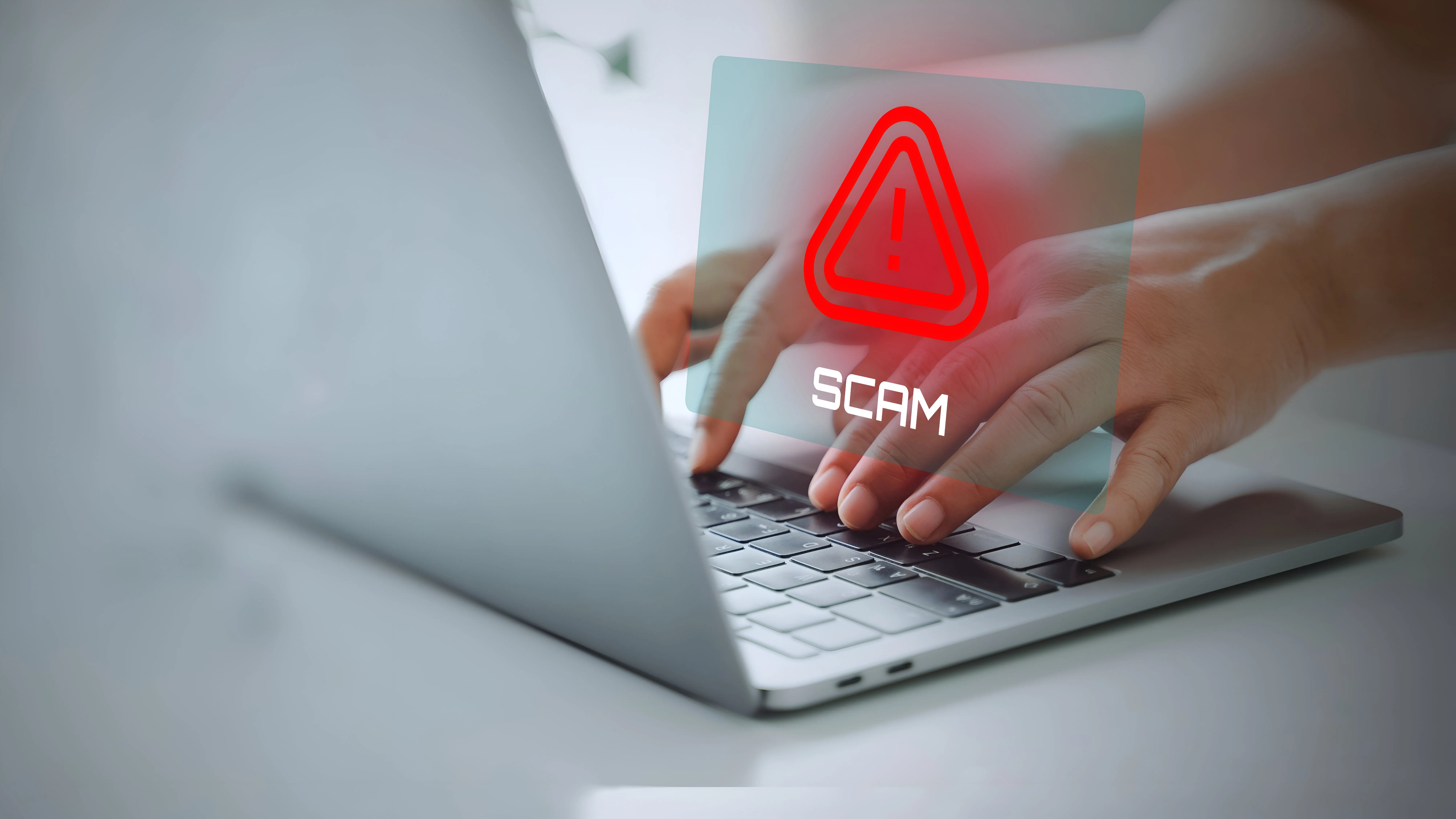 Hands typing on a laptop with a large SCAM warning alert.