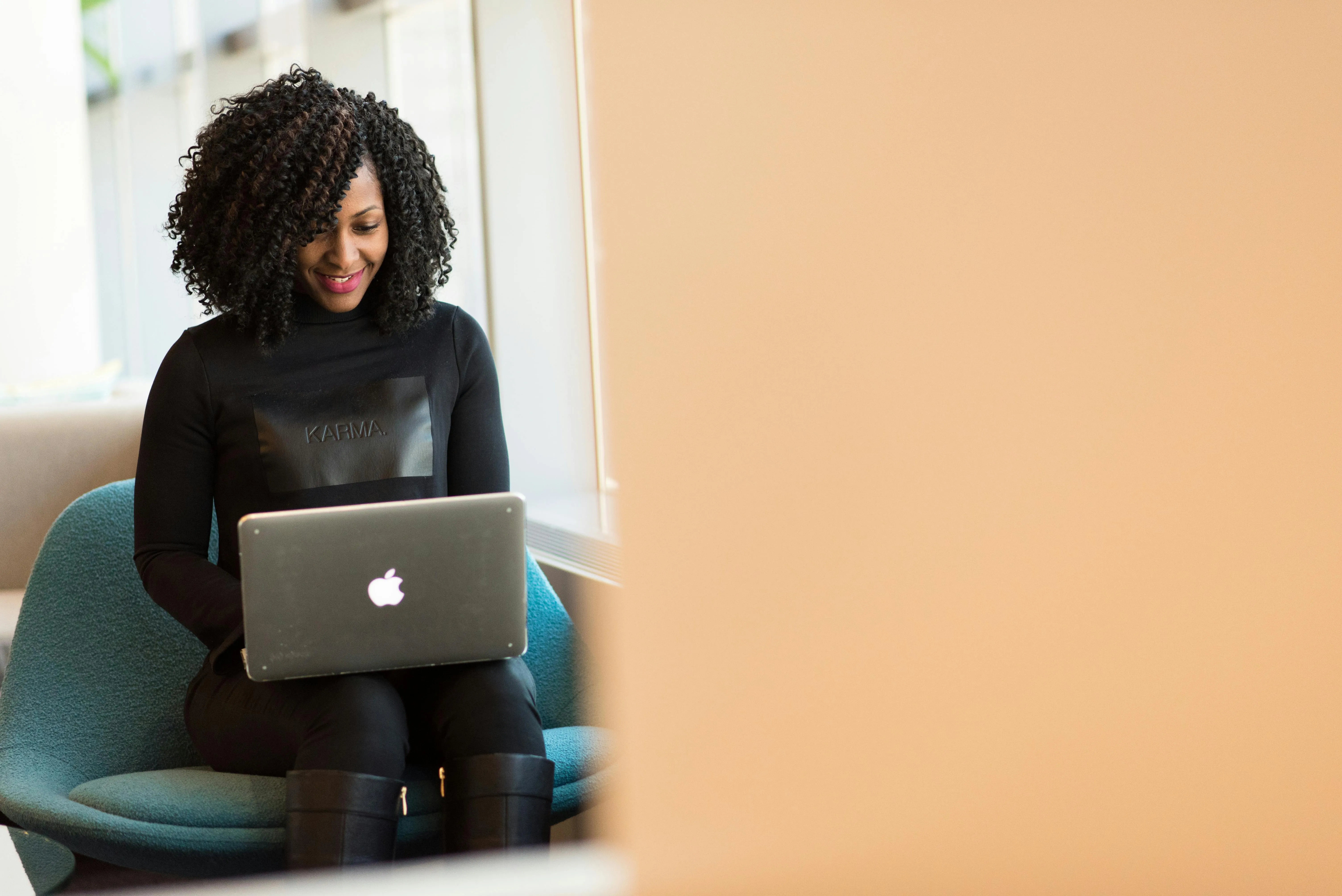 Professional woman in Karma apparel smiling while using silver MacBook laptop.