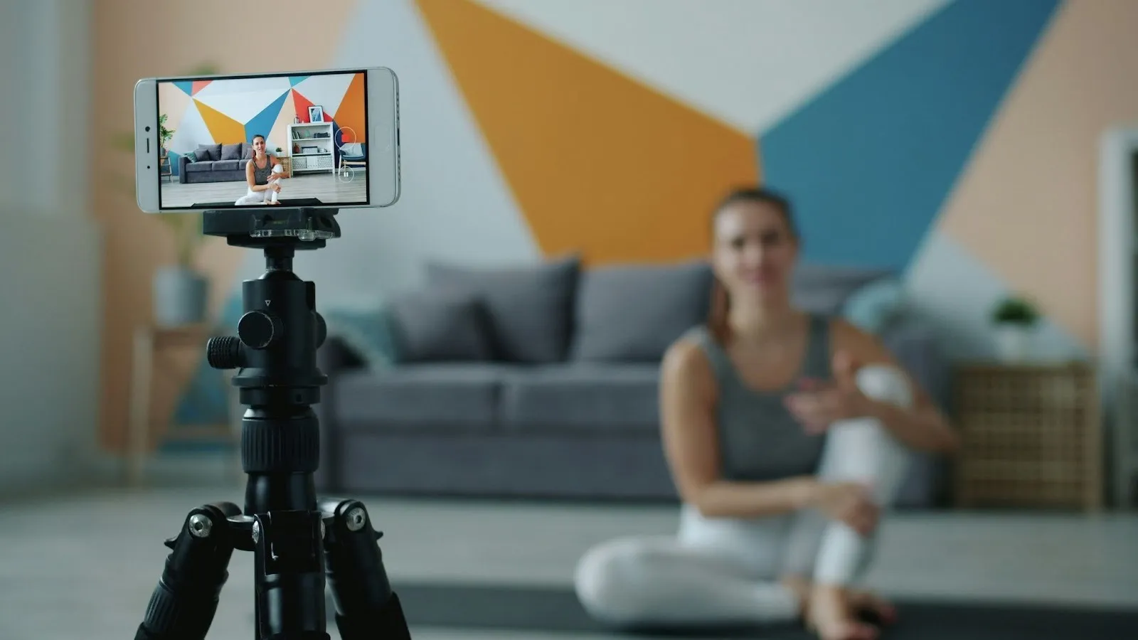 Woman recording a yoga tutorial video on a smartphone mounted on a tripod at home.