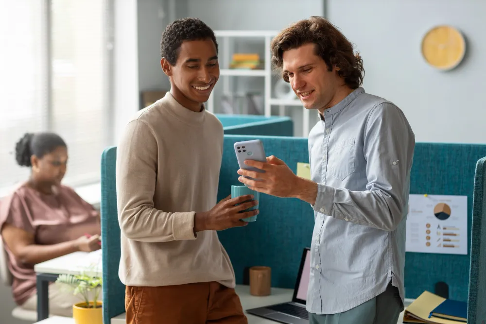 Two smiling coworkers viewing phone together in bright office space