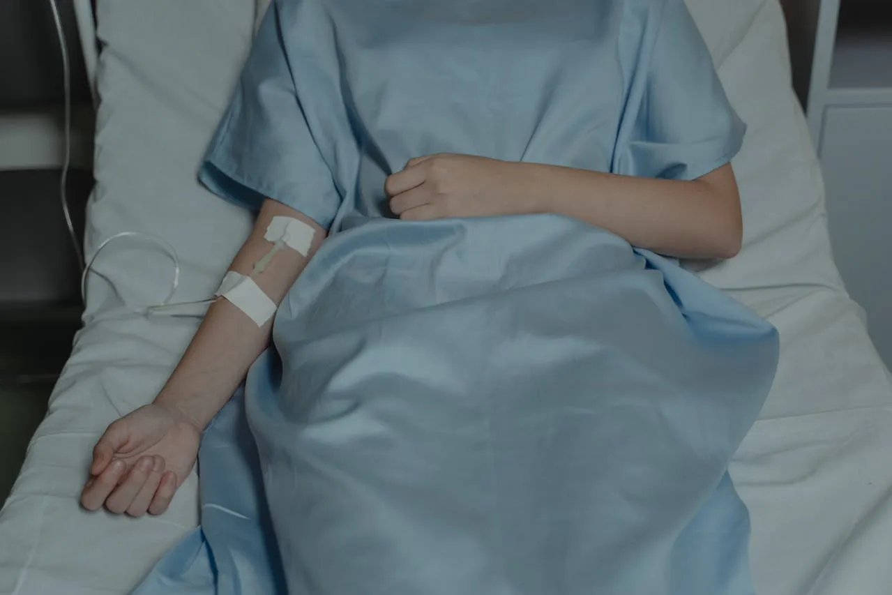 Patient’s arm with IV catheter and hospital gown during treatment.