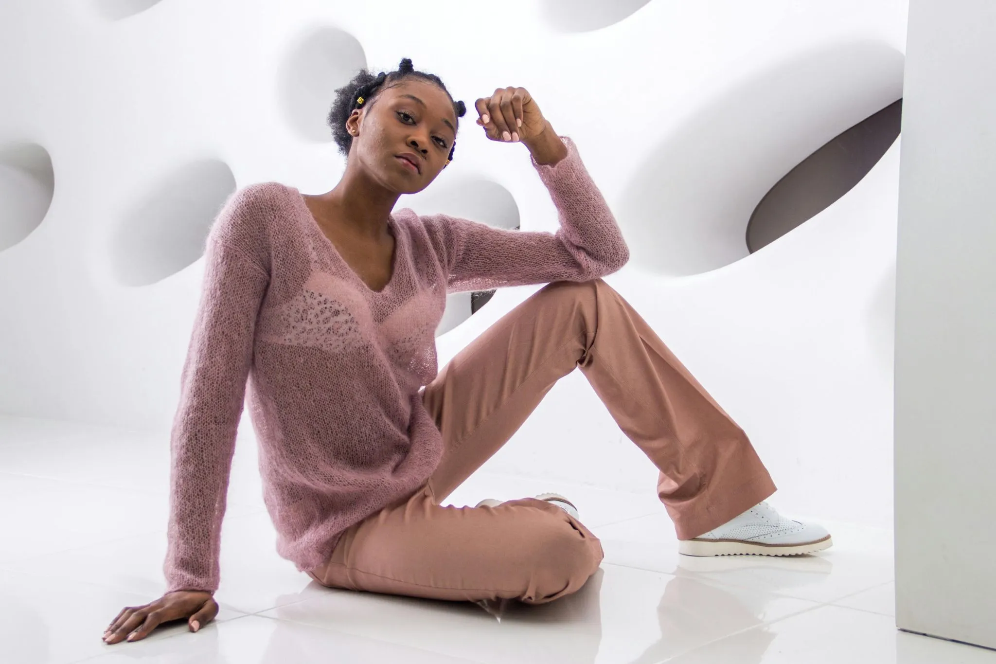 Elegant black woman in pink knit sweater posing confidently in modern studio setting.