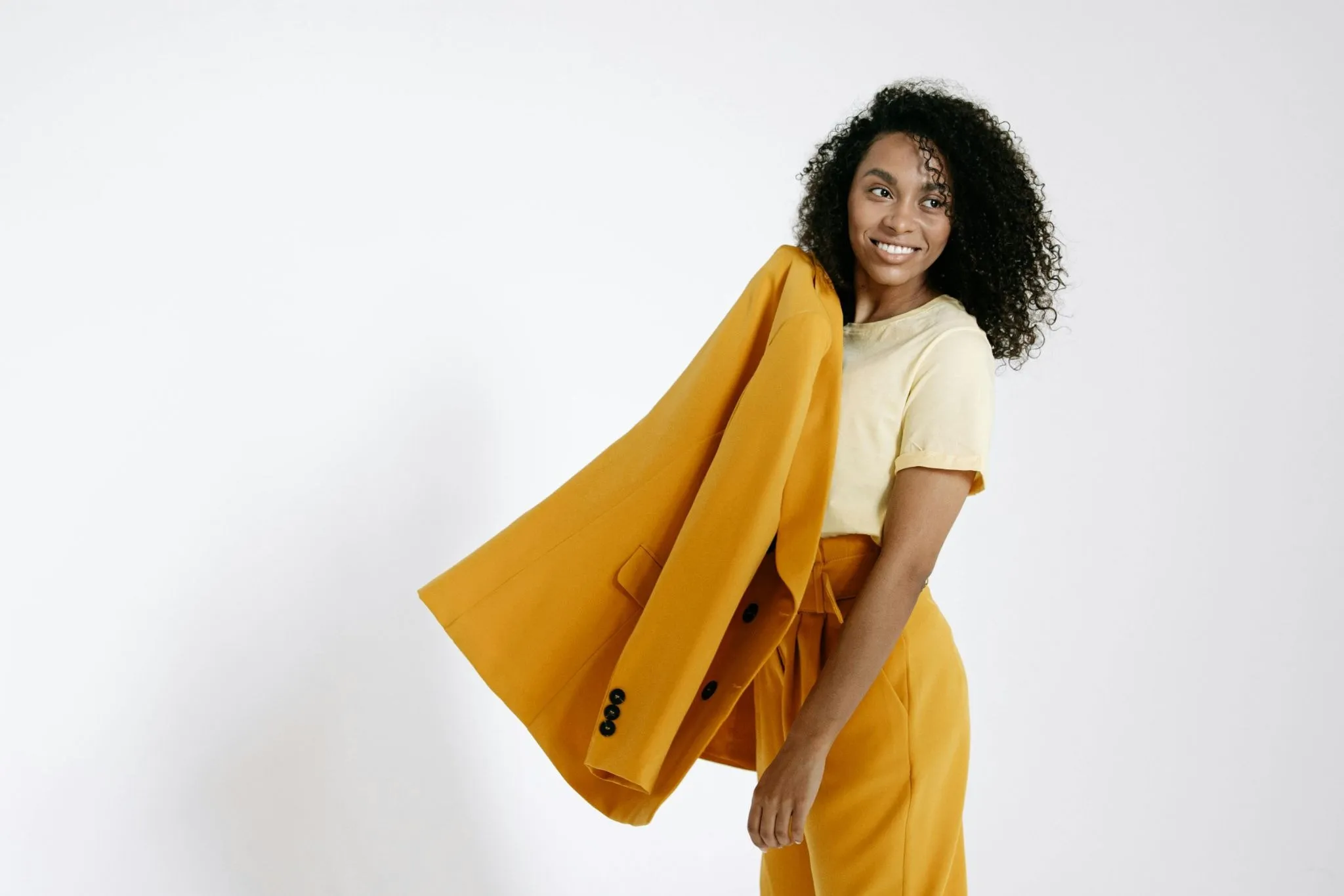 Stylish woman with curly hair wearing a vibrant yellow blazer and matching trousers.